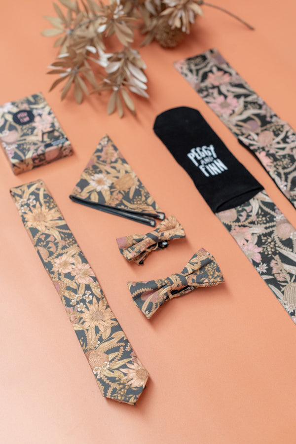 The Byron Banksia collection features men's accessories with prints of Australian plants like Banksias and Waratah, set against a charcoal background. This range combines classic style with a natural motif