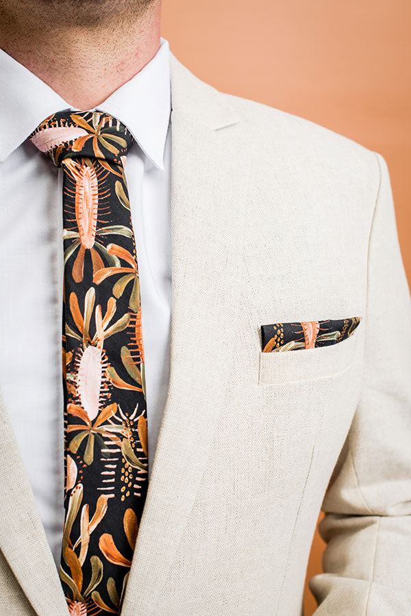 Stylish tie crafted from cotton, adorned with leafy designs in tones of burnt orange, sage green, and terracotta on a black background